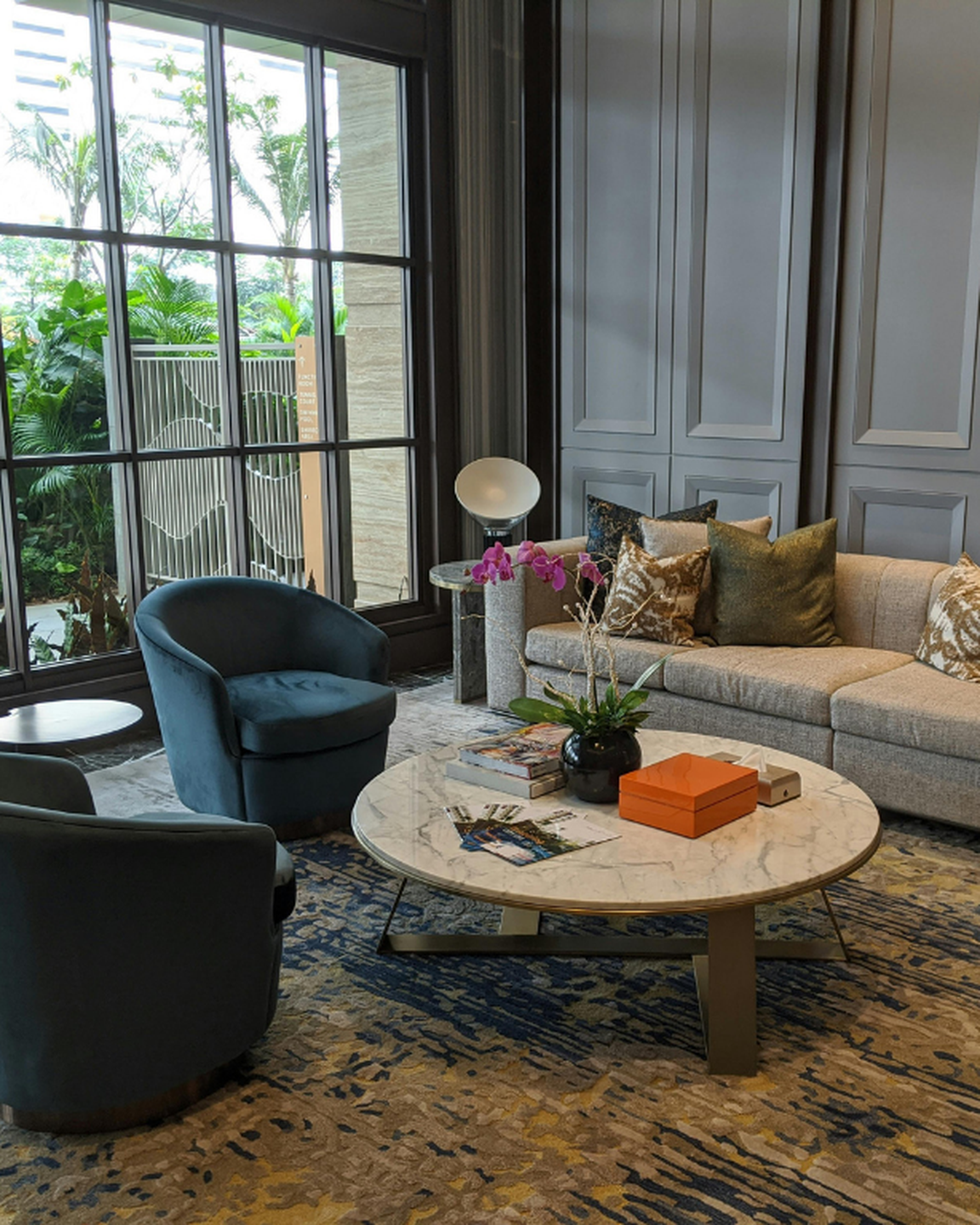 Refined hotel lounge interior with teal velvet chairs, marble coffee table, cream sofa, and tall paneled windows